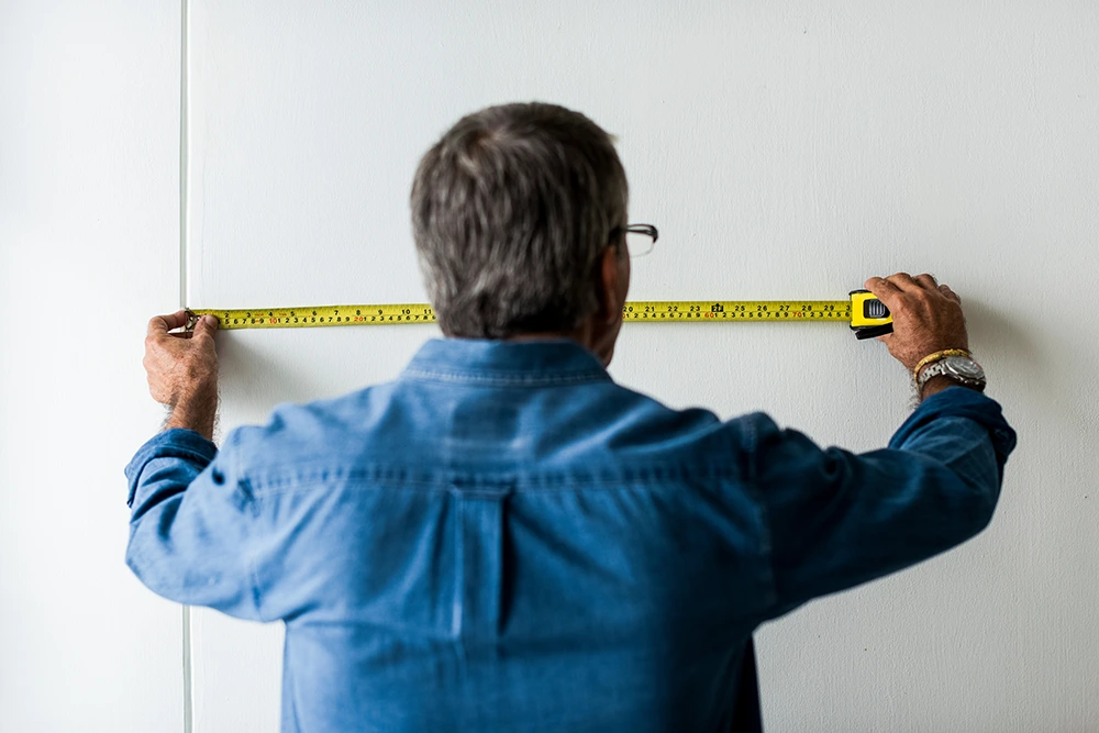 an image of a man measuring his wall for a media wall
